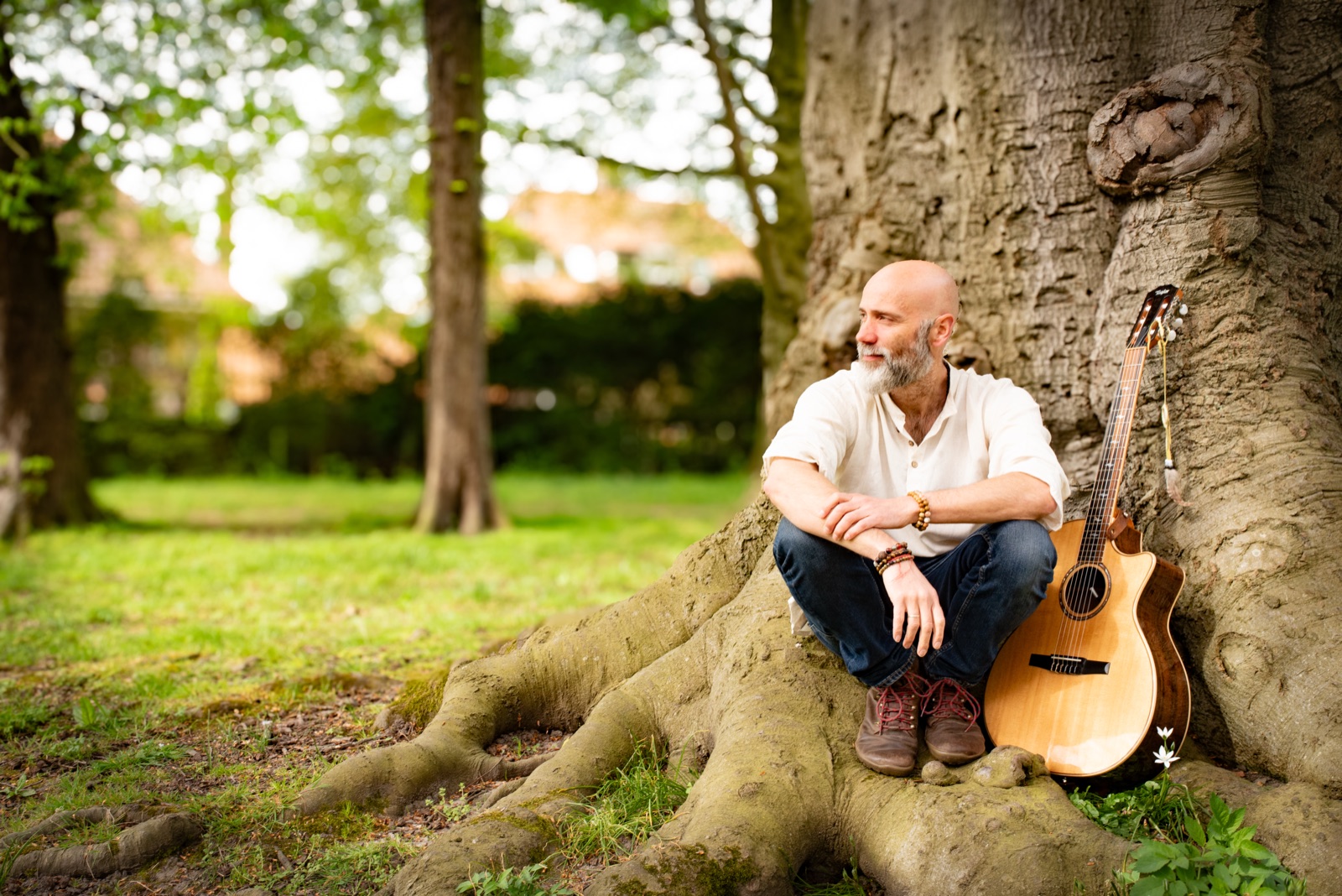 Derk de Geus sitting with his acoustic guitar at the foot of a large tree in a park